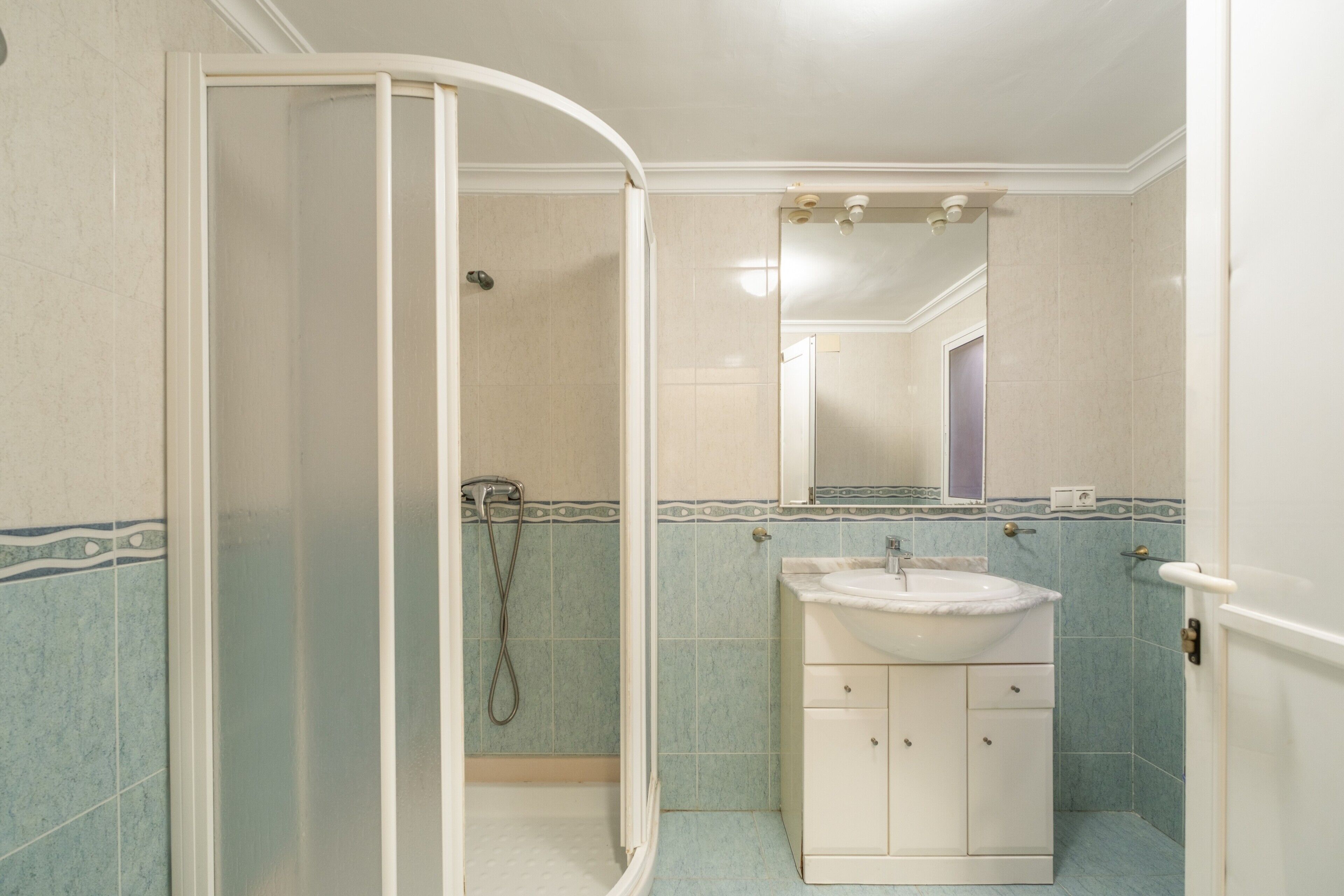 Baño con cabina de ducha, lavamanos y espejo.