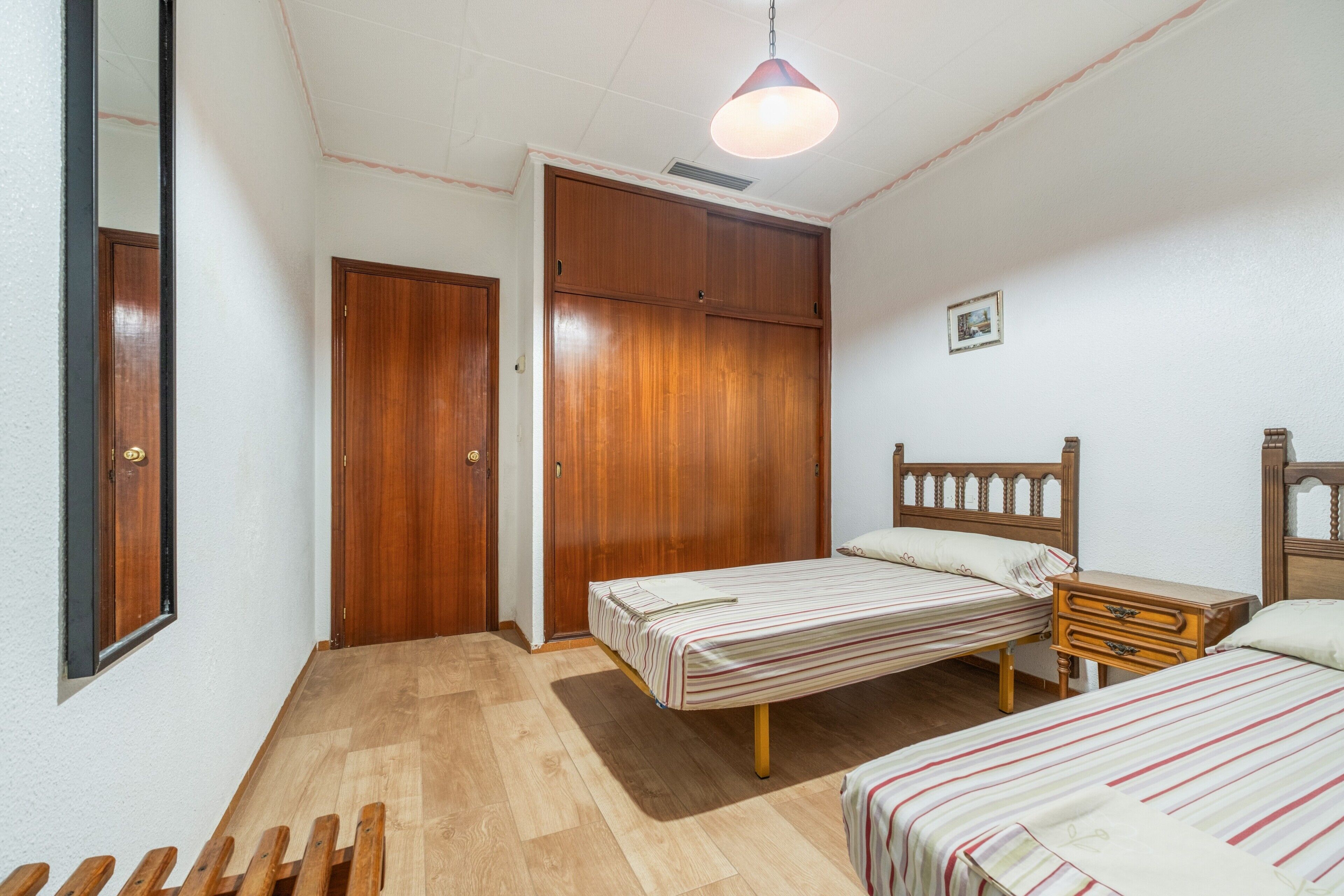 Un dormitorio con un armario de madera, una cama con colcha a rayas y una mesita de noche.