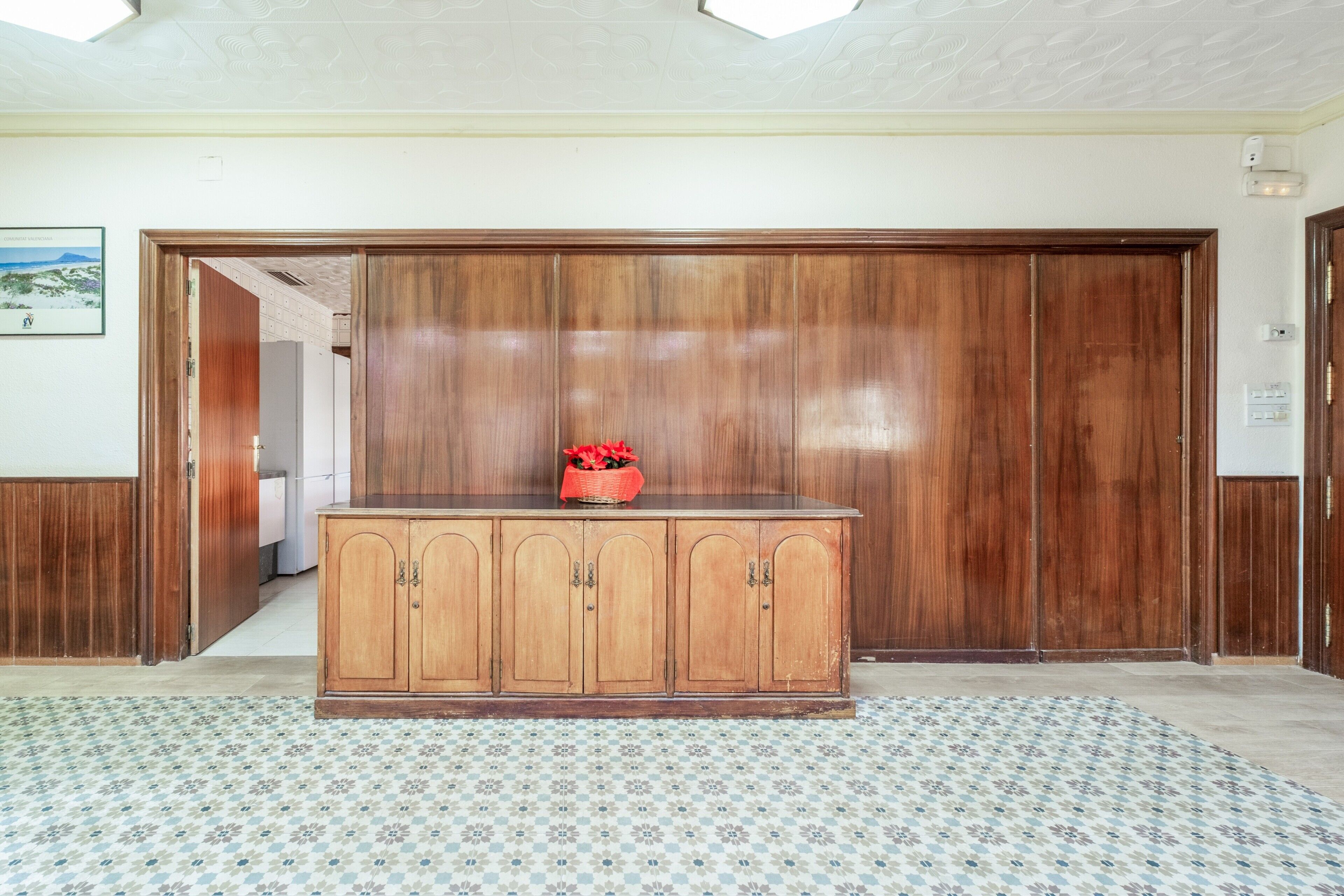 Une pièce avec un meuble en bois, un parquet à motifs et une porte donnant sur une autre pièce.