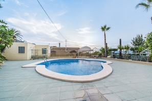 A swimming pool with a curved edge, surrounded by a paved area with a fence, and a building with a dome-shaped structure in the background.