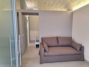 A room with a brown sofa, a glass door, and a tiled floor. - Furnished studio apartment for rent on the ground floor. (Taranto)
