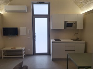 A compact living space with a kitchenette, a television, a door with a view, and a small seating area. - Furnished studio apartment for rent on the ground floor. (Taranto)