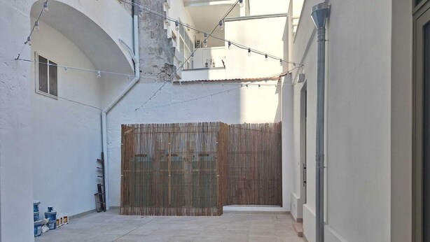A narrow courtyard with a tiled floor, a bamboo fence, and a string of lights.