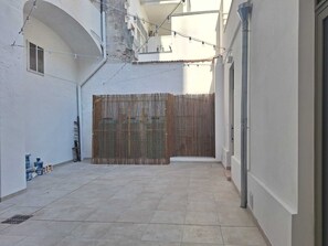 A narrow courtyard with a tiled floor, a bamboo fence, and a string of lights. - Furnished studio apartment for rent on the ground floor. (Taranto)
