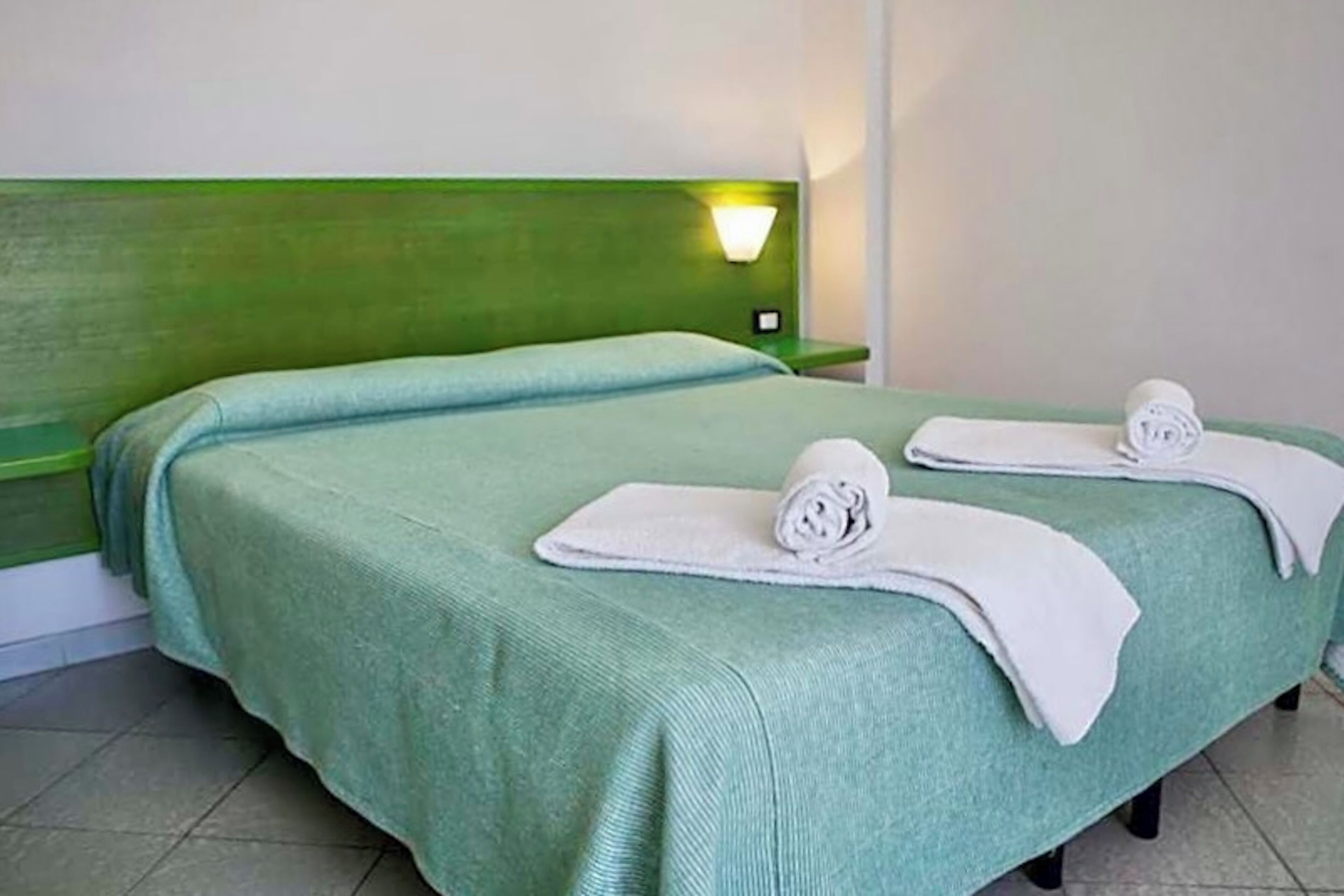 A double bed with green bedding and two rolled towels.