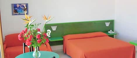 Een kamer met een groen bed, een oranje bed, een ronde tafel met een stoel, en een vaas met bloemen.