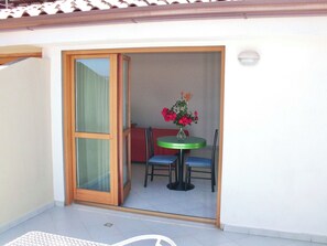 A room with a sliding glass door leading to an outdoor area with a table and chairs, a vase with flowers, and a red sofa.