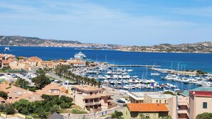 Un port de plaisance sur la côte, avec des bateaux amarrés, un ciel dégagé et des bâtiments au premier plan.