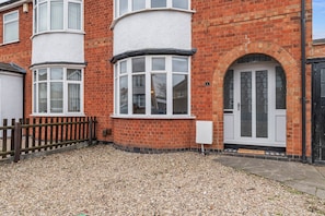 A red brick building with white-framed windows, a black door, and a gravel driveway. - 4-Bed House | Leicester | Driveway Parking (Leicester)