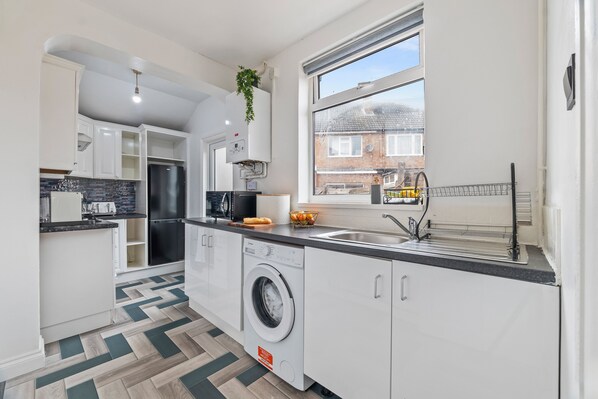 A modern kitchen with a built-in washing machine, a large window, and a view of the outside. - 4-Bed House | Leicester | Driveway Parking (Leicester)