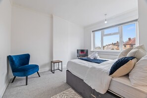 A bedroom with a bed, a chair, a TV, and a window. - 4-Bed House | Leicester | Driveway Parking (Leicester)