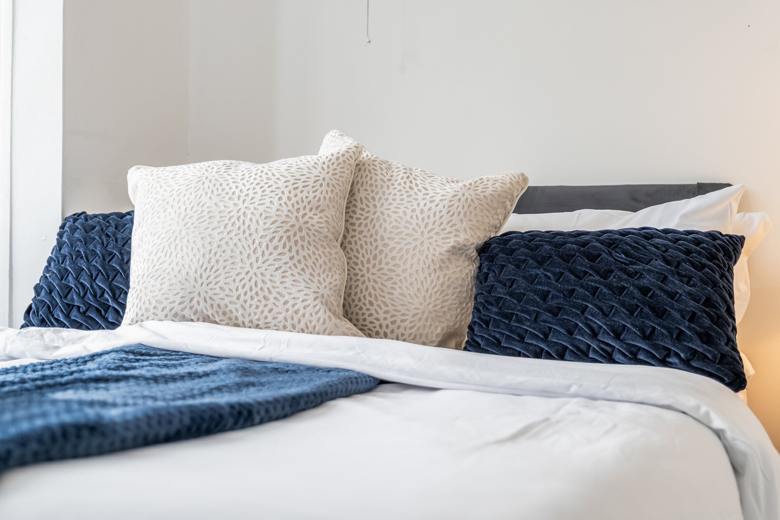 A bed with a white and blue duvet, two white pillows, and a dark blue pillow.