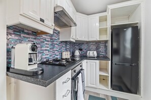 A modern kitchen with white cabinets, a black countertop, a stainless steel refrigerator, a coffee machine, and a toaster. - 4-Bed House | Leicester | Driveway Parking (Leicester)