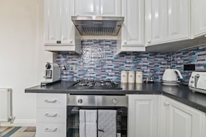 A modern kitchen with white cabinets, a gas stove, a coffee maker, and a toaster. - 4-Bed House | Leicester | Driveway Parking (Leicester)
