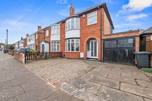 A residential street with houses, a paved sidewalk, and a gravel area. - 4-Bed House | Leicester | Driveway Parking (Leicester)