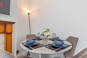 A dining area with a round table set for four, featuring blue dinnerware and a vase with white flowers. - 4-Bed House | Leicester | Driveway Parking (Leicester)