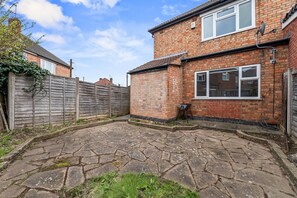A brick house with a stone patio, a wooden fence, and a satellite dish. - 4-Bed House | Leicester | Driveway Parking (Leicester)