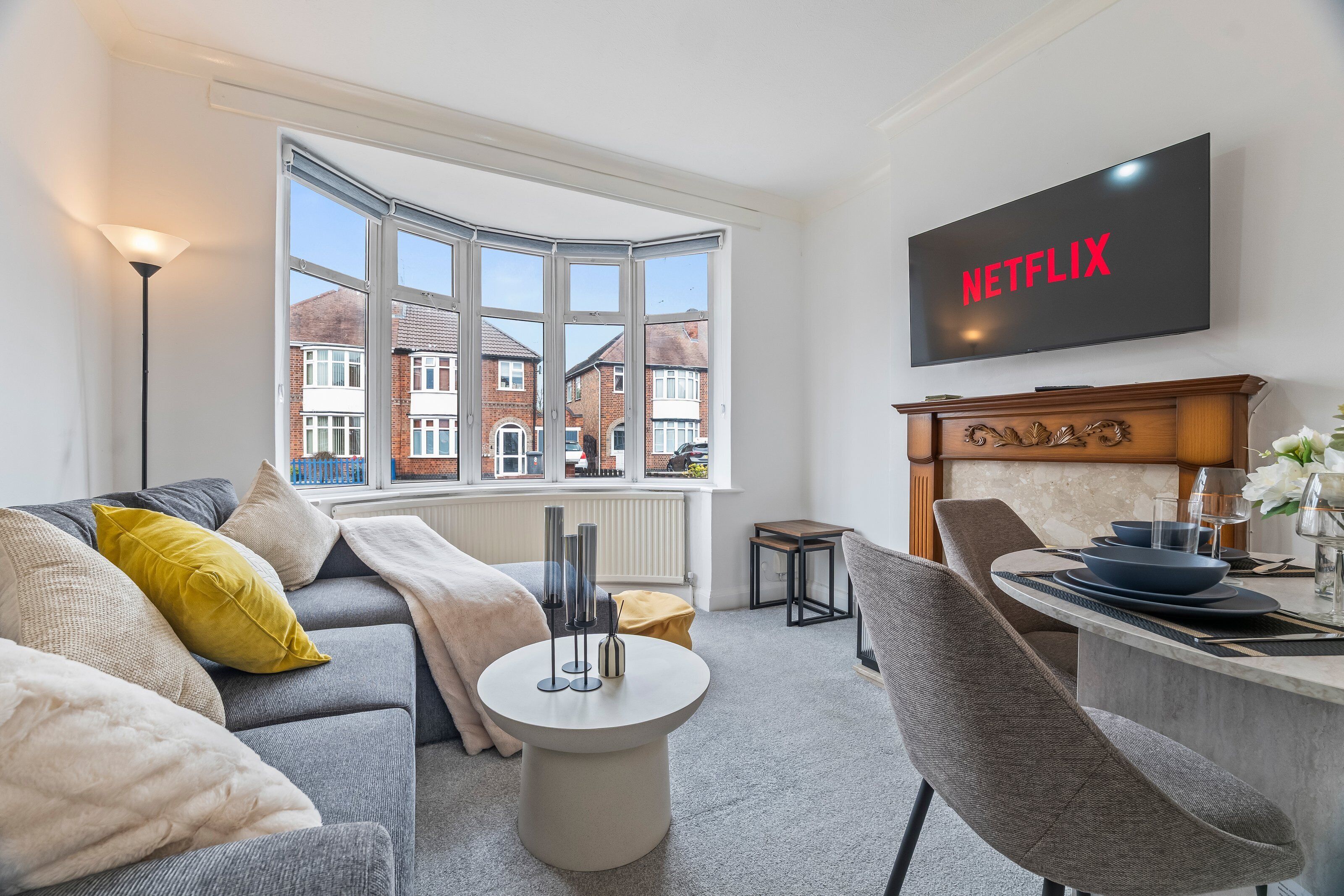 Ein modernes Wohnzimmer mit einer Couch, einem Couchtisch und einem Essbereich mit Stühlen und einem Tisch. Ein großes Fenster bietet Blick auf die Nachbarschaft.