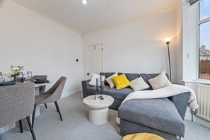 A modern living room with a grey sofa, a dining table with chairs, and a small round table with decorative items. - 4-Bed House | Leicester | Driveway Parking (Leicester)