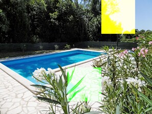 Una piscina con agua azul cristalina, rodeada por un patio de piedra y abundante vegetación.