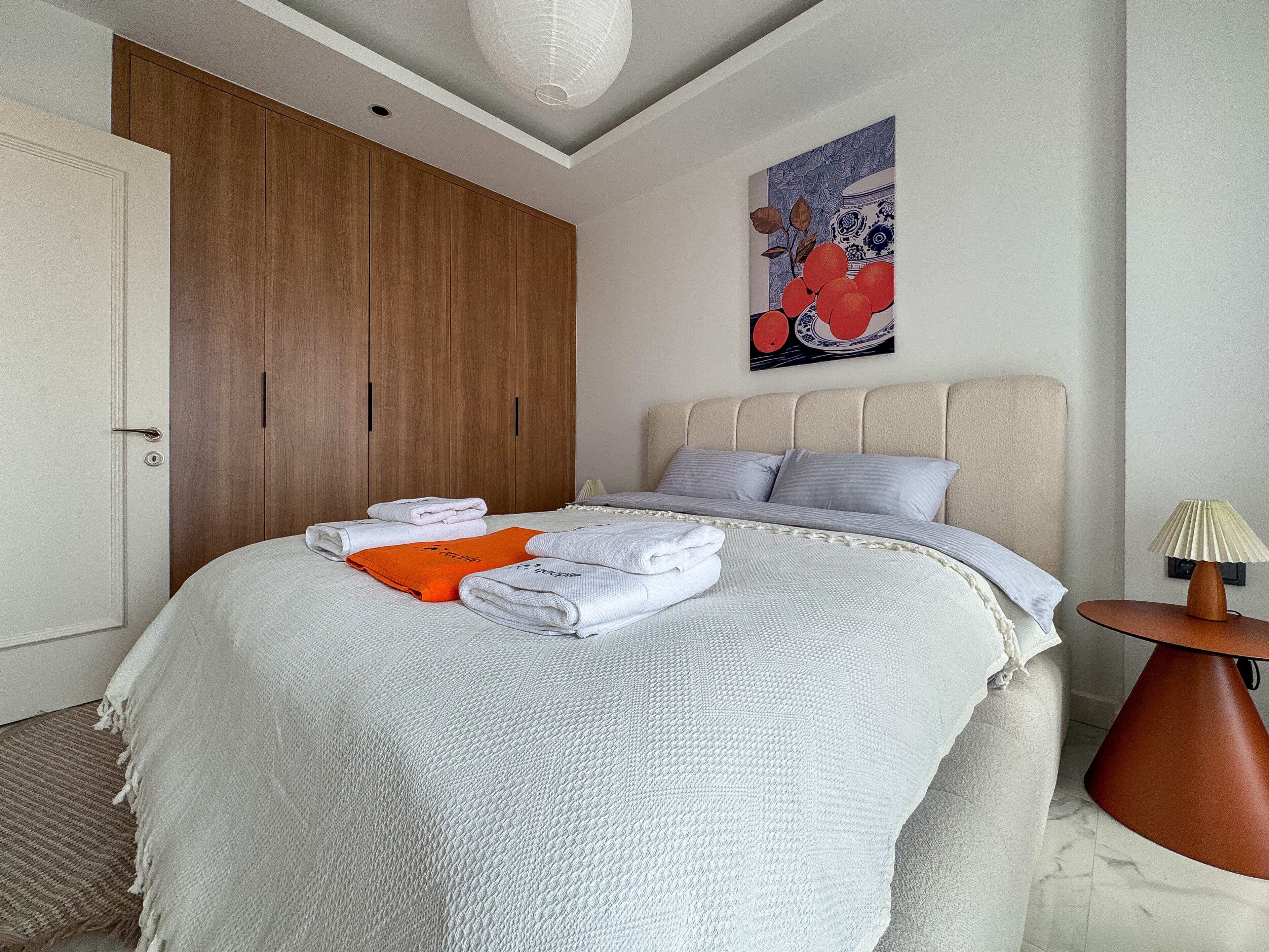 Un dormitorio con cama, armario de madera, cuadro y mesita de noche con lámpara.