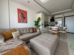 A modern living room with a sofa, coffee table, and a dining area with chairs. - Qoople Elize A39 - Cozy 1-bedroom apartment in Alanya (Alanya)