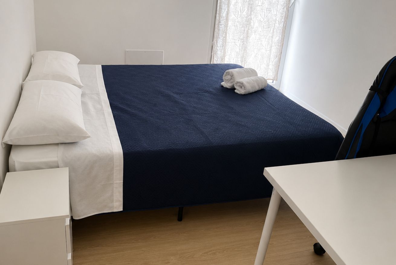 Una habitación de hotel con una cama, un escritorio blanco y un ventanal con cortinas.