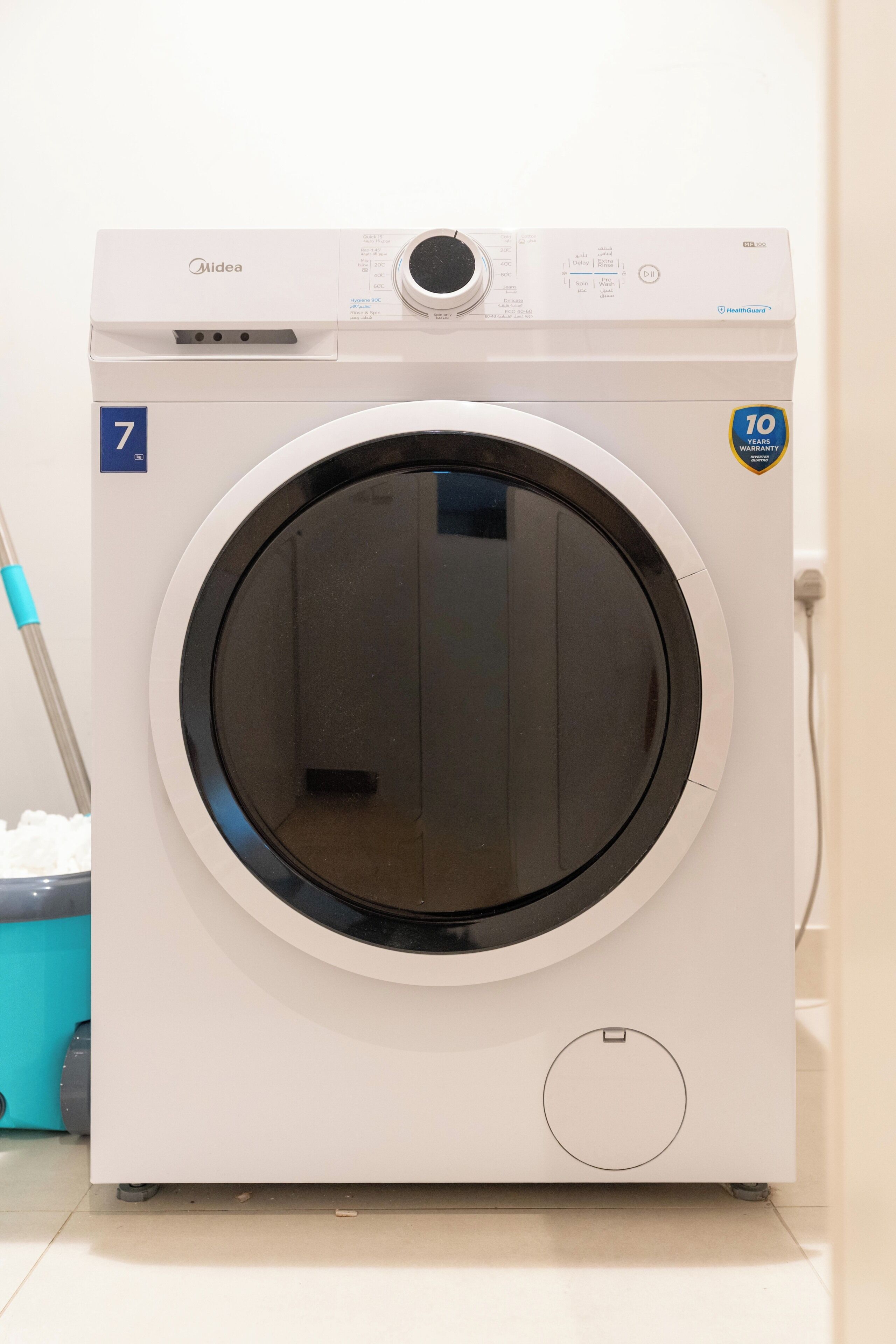 A front-loading white washing machine with a digital display, a 10-year warranty badge, and a small circular vent.