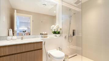 A modern bathroom with a glass shower enclosure, a wooden vanity, and a toilet.