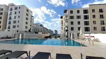 A swimming pool with lounge chairs, surrounded by multi-story residential buildings.