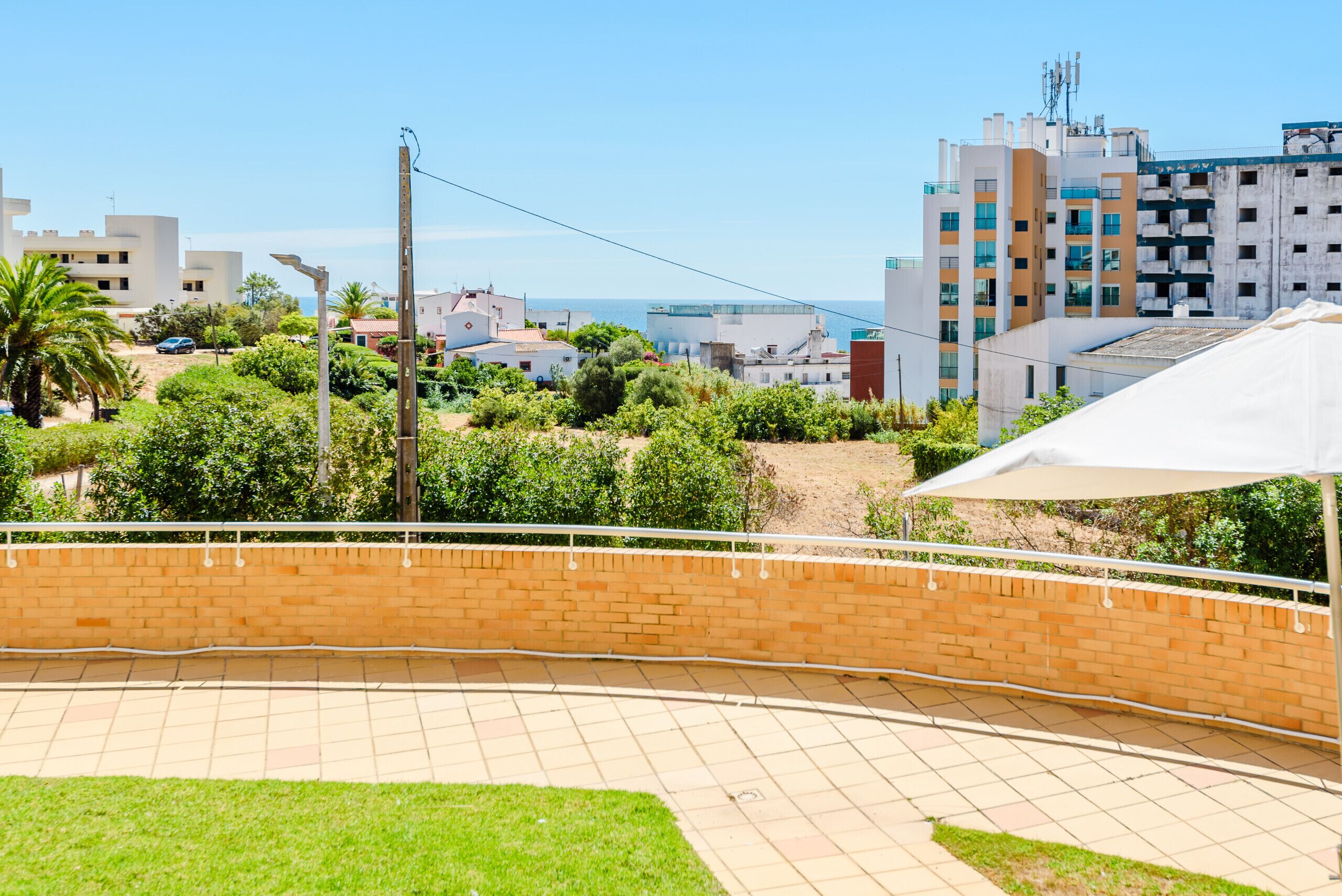 Um pátio com parede de tijolos, um guarda-sol branco e vista para o mar e edifícios.