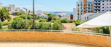 A courtyard with a brick wall, a white umbrella, and a view of the sea and buildings.