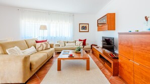 Uma sala de estar com sofá, mesa de centro, televisão e armário de madeira.