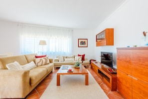 A living room with a sofa, coffee table, TV, and wooden cabinet. - Praia Dona Ana Apartment (Lagos)