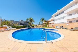 A swimming pool with multiple lanes, surrounded by lounge chairs and a brick wall. - Praia Dona Ana Apartment (Lagos)