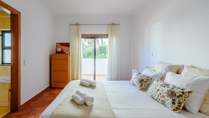 Quarto com cama, almofadas, cômoda e janela com cortinas.