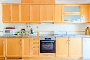 A kitchen with wooden cabinets, a microwave, a kettle, and a dishwasher. - Praia Dona Ana Apartment (Lagos)