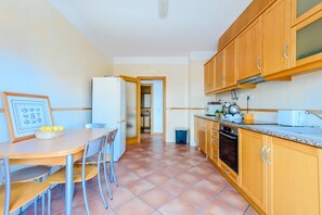 A compact kitchen with wooden cabinets, a dining table with chairs, and a tiled floor. - Praia Dona Ana Apartment (Lagos)