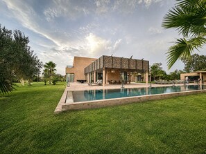 A modern building with a swimming pool, outdoor seating, and lush greenery. - Exceptional villa overlooking the Amelkis Golf Course - 6 bedrooms, hammam, and indoor pool (Marrakech)