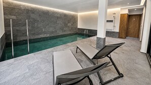 A modern indoor pool area with a clear pool, two lounge chairs, and a wooden door. - Exceptional villa overlooking the Amelkis Golf Course - 6 bedrooms, hammam, and indoor pool (Marrakech)