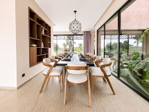 A modern dining area with a long table, wooden chairs, and a geometric pendant light. - Exceptional villa overlooking the Amelkis Golf Course - 6 bedrooms, hammam, and indoor pool (Marrakech)