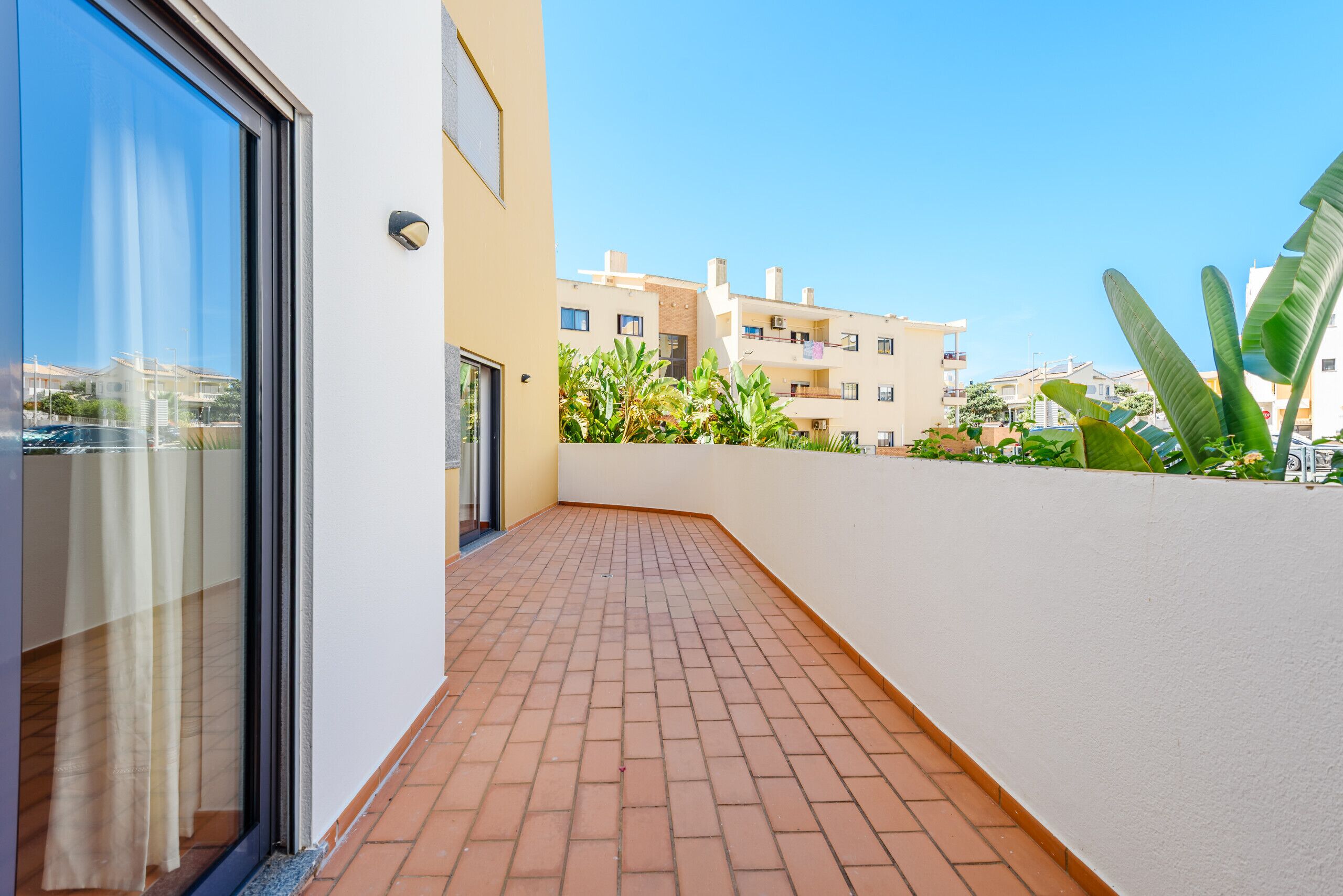 A narrow outdoor corridor with a tiled floor, a glass door, and a white wall.