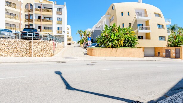 A street with a row of modern buildings, a clear sky, and parked cars. - Apartment Praia Dona Ana (Lagos)
