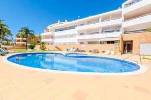A swimming pool with lounge chairs, a brick wall, and a multi-story building with balconies. - Apartment Praia Dona Ana (Lagos)
