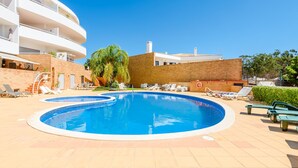 A swimming pool with lounge chairs and a multi-story building in the background. - Apartment Praia Dona Ana (Lagos)