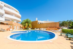 A swimming pool with lounge chairs and a multi-story building in the background. - Apartment Praia Dona Ana (Lagos)