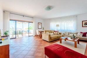 A spacious living room with a sofa, a red armchair, a coffee table, and a dining area with chairs and a table. - Apartment Praia Dona Ana (Lagos)