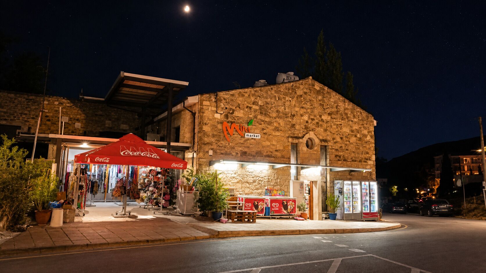 A stone building with a Coca-Cola branded outdoor umbrella, a sign reading 'market,' and a refrigerated display.