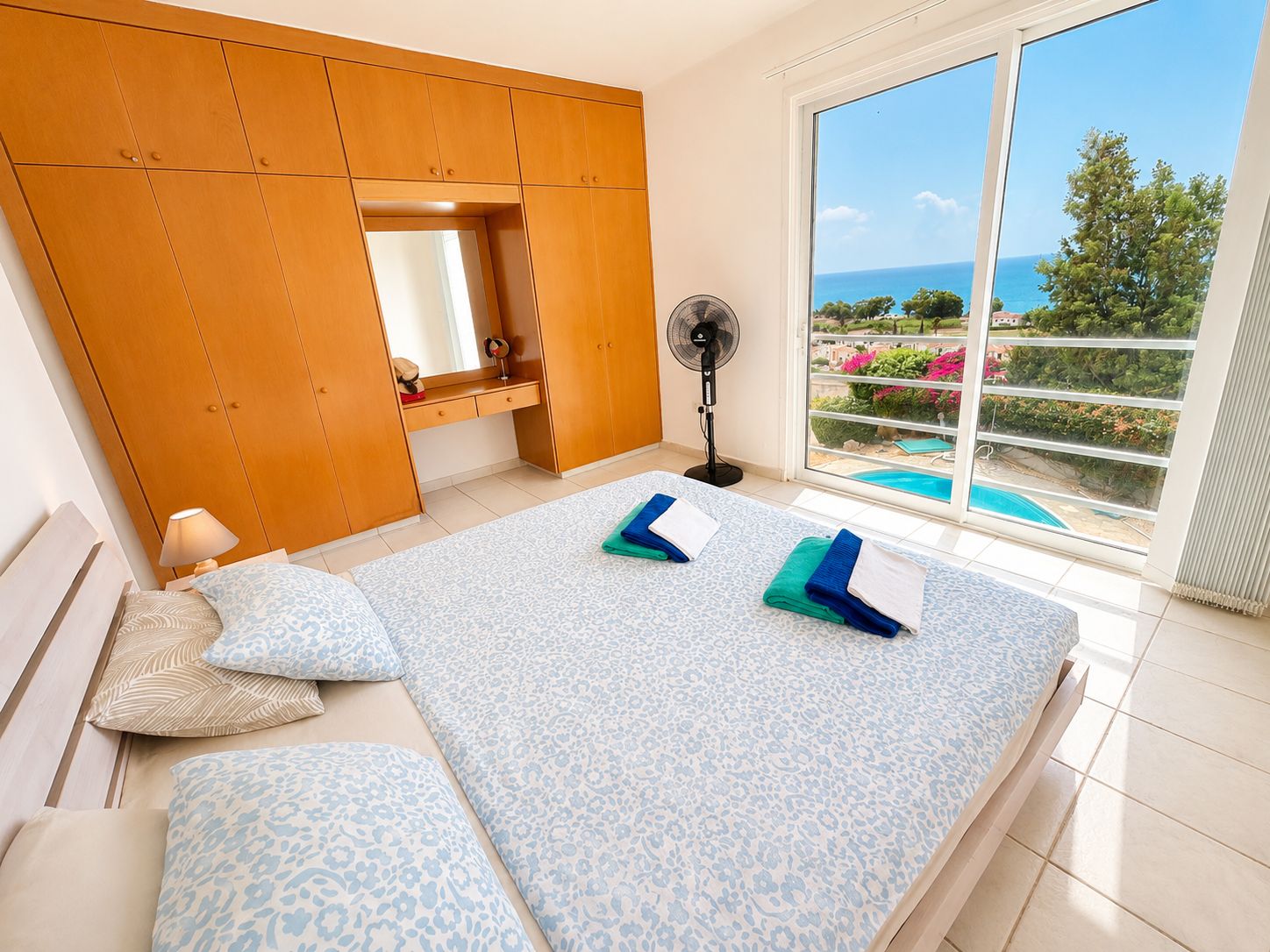 A bedroom with a large bed, a wardrobe, a fan, and a view of the sea.