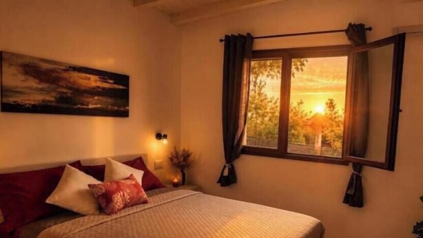 Ein Schlafzimmer mit Bett, einem Fenster mit Vorhängen, einer Wandleuchte und einem Bild.